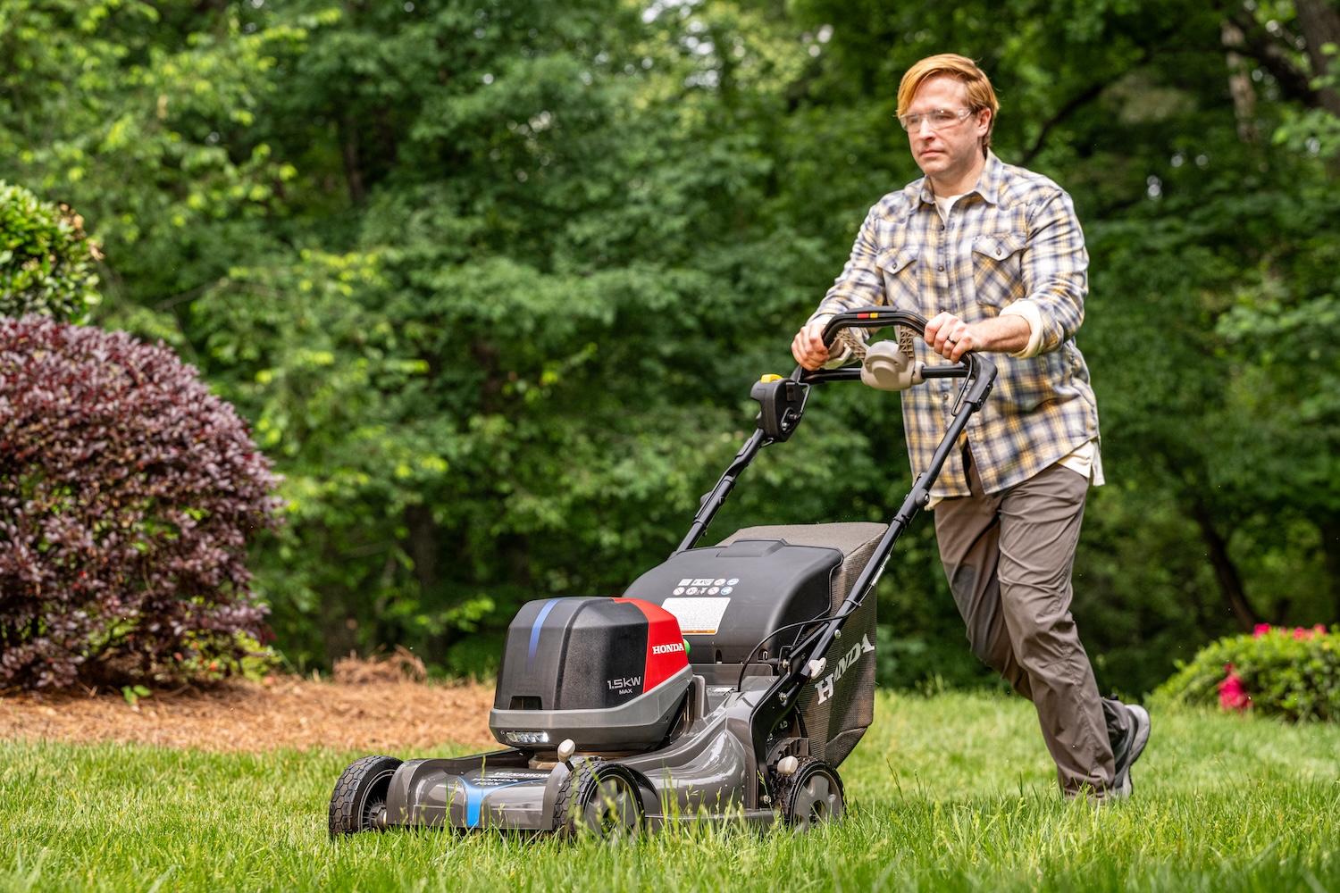 Homeowner mowing a green lawn with a Honda battery-powered walk-behind mower