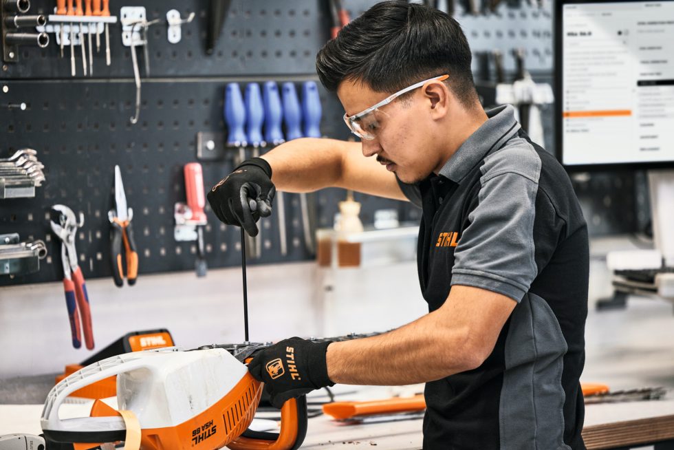 Technician servicing a Stihl hedge trimmer on a workbench in the service shop